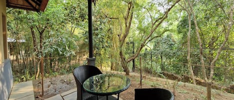 An outdoor seating area with a glass table and wicker chairs, surrounded by a forested landscape.