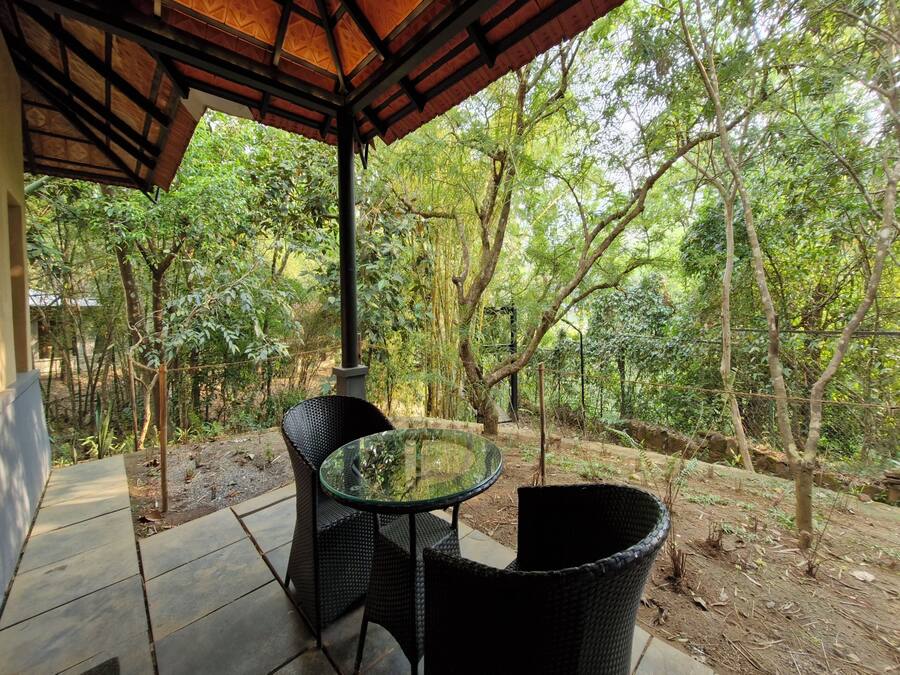 Un espacio al aire libre con una mesa de vidrio y sillas de mimbre, rodeado por un paisaje boscoso.