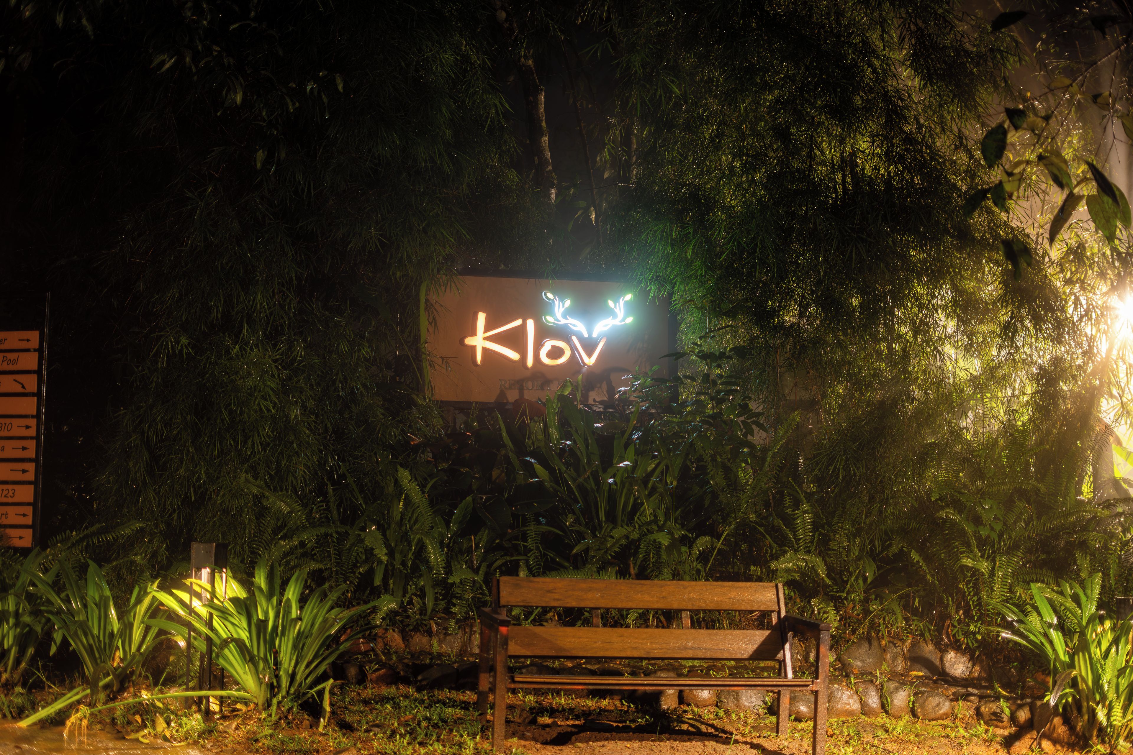 A bench in a garden with a neon sign in the background.