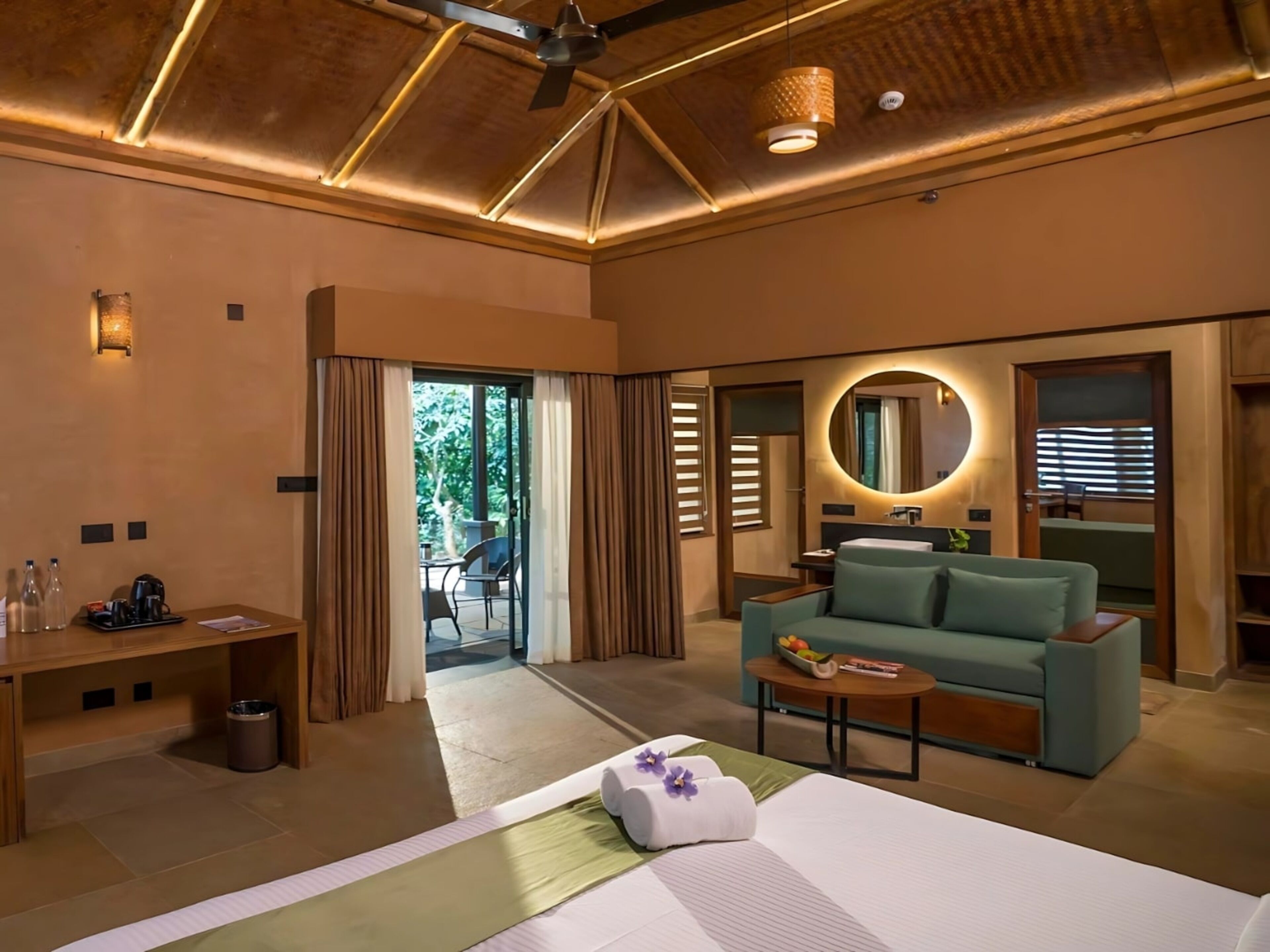 A modern hotel room with a bed, a sofa, a small table, a desk, and a bathroom visible through an open door.