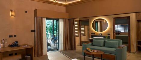 A modern hotel room with a bed, a sofa, a small table, a desk, and a bathroom visible through an open door.