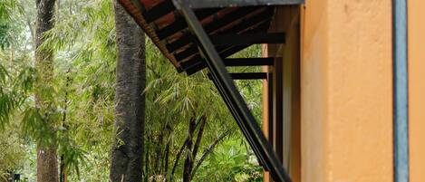 Un bâtiment à la façade jaune, doté d’un auvent en bois à lattes et entouré d’une végétation luxuriante.