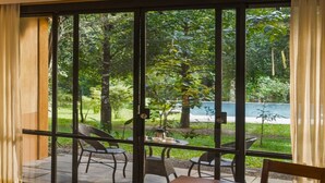 A room with a large sliding glass door leading to an outdoor area with chairs and a table. - Klov Resort & Spa (Mananthavady)