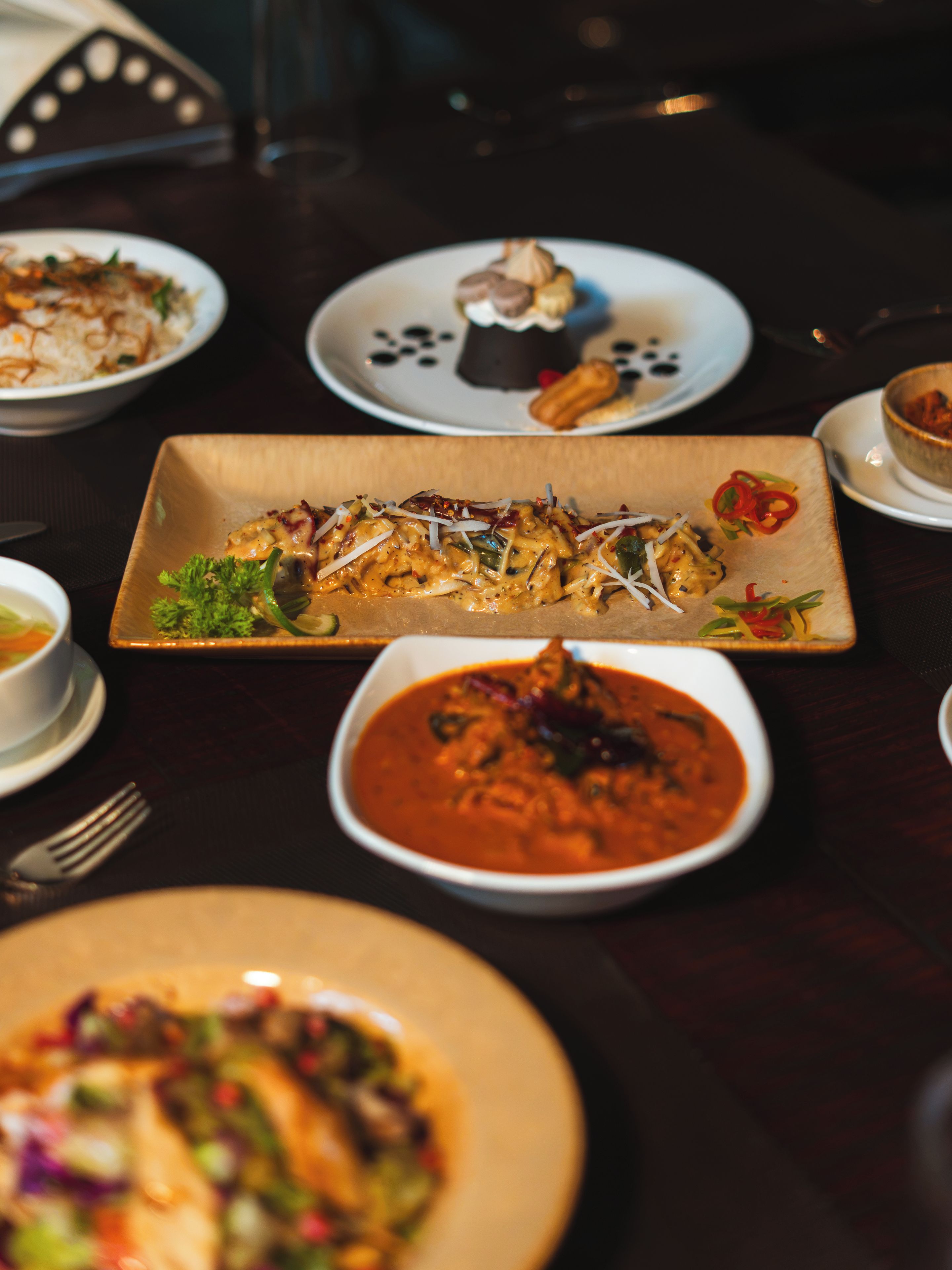 A variety of dishes on a table, including a fish dish, a bowl of soup, and other plates with different foods.