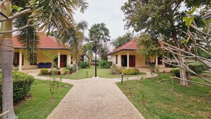 A pathway leading to two identical buildings with red-tiled roofs, surrounded by lush greenery and palm trees. - Beautiful bungalow with shared outdoor pool and 2 km from the sandy beach (Tambon Cha-am)