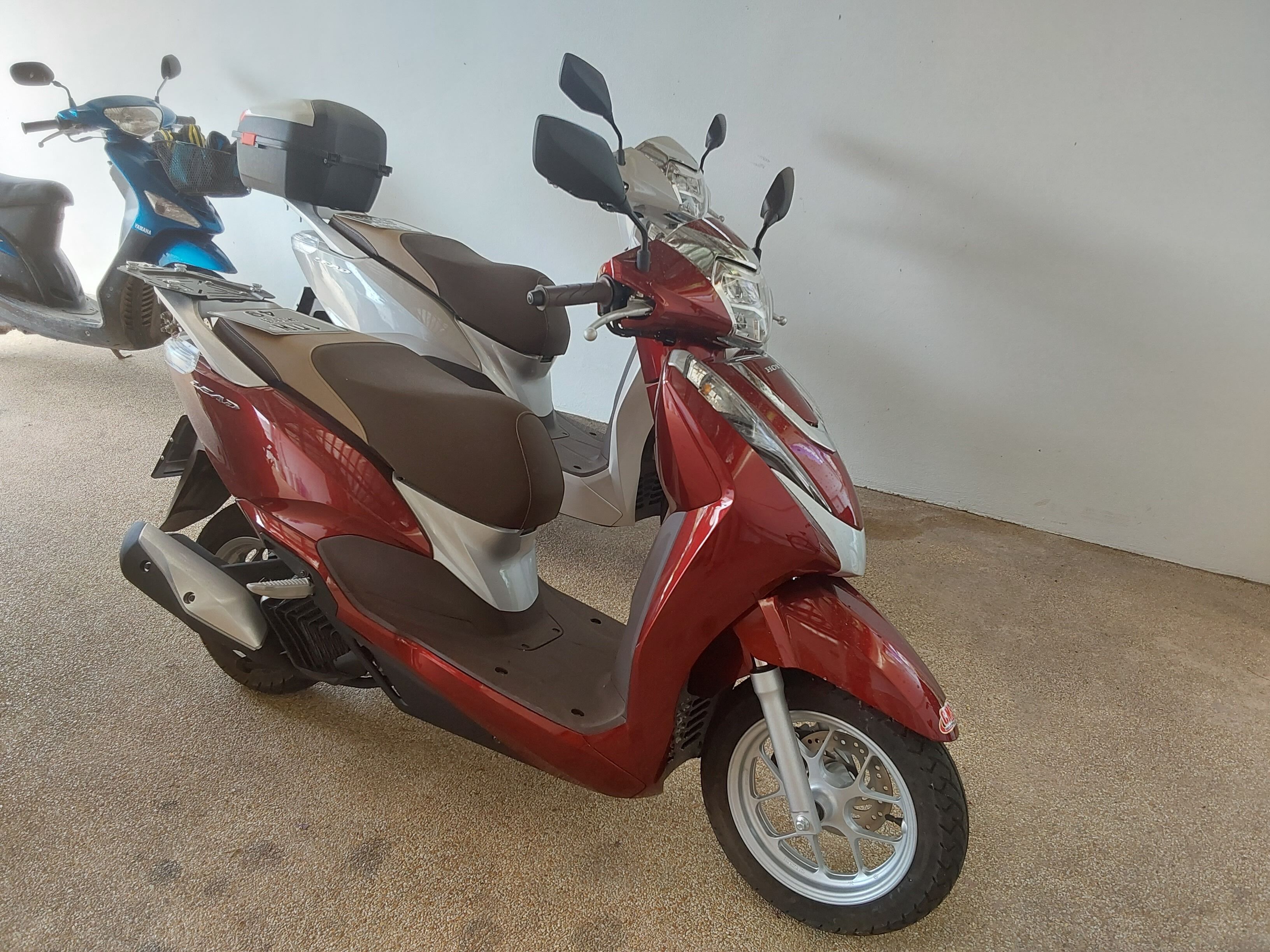 A red scooter with a brown seat and a basket on the front.