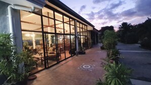A building with large glass windows and doors, a tiled patio, and potted plants. - Beautiful bungalow with shared outdoor pool and 2 km from the sandy beach (Tambon Cha-am)