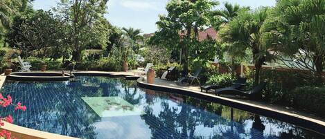 A swimming pool with tiled edges, surrounded by palm trees and lounge chairs.
