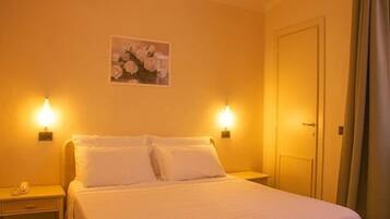 A hotel room with a bed, two bedside lamps, a door, and a wall-mounted picture.