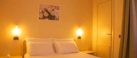 Habitación de hotel con cama, dos lámparas de noche, una puerta y un cuadro colgado en la pared.