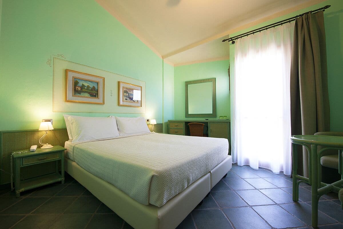 Una habitación con cama, mesitas de noche, escritorio, silla, espejo y dos cuadros en la pared.
