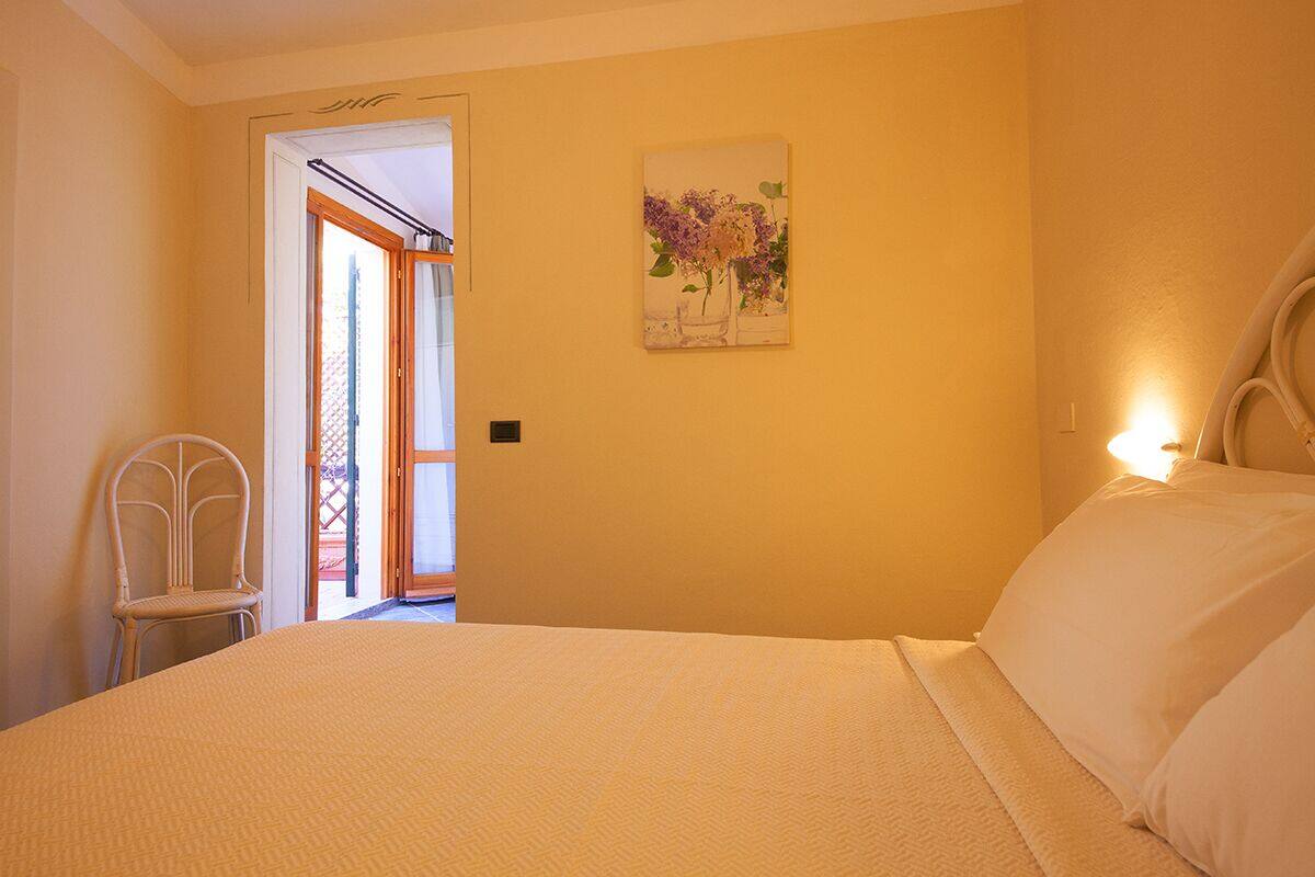Un dormitorio con cama, una silla, una puerta que da a un espacio exterior y una lámpara fijada a la pared.