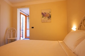 A bedroom with a bed, a chair, a door leading to an outdoor area, and a wall-mounted light fixture. - Hotel Danila (Scaglieri)