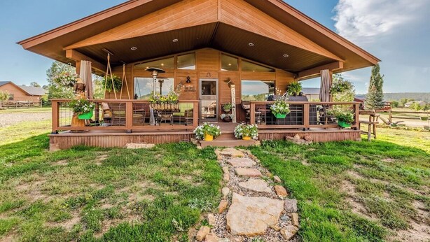 Un bâtiment moderne en bois doté d’un grand patio couvert, d’un espace extérieur aménagé pour s’asseoir et de plantes en pot.