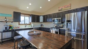 Une cuisine moderne avec des meubles de couleur sombre, des appareils en acier inoxydable et un îlot central en bois doté de tabourets.