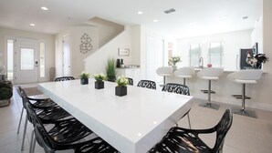 A modern kitchen with white countertops, black chairs, and a large island with plants. - Contemporary Disney VacationHome (Kissimmee)