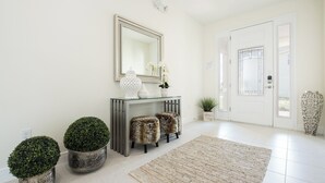 A clean, modern entryway with a glass console table, decorative urns, and a mirror above. - Contemporary Disney VacationHome (Kissimmee)