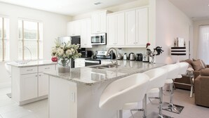 A modern kitchen with white cabinets, a granite countertop, and a central island with bar stools. - Contemporary Disney VacationHome (Kissimmee)