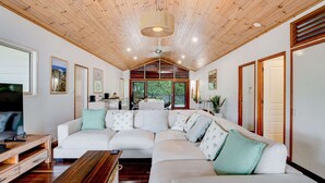 Una sala de estar moderna con un sofá modular, techo de madera y ventanas amplias.