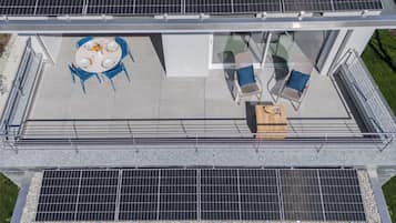 Une terrasse sur le toit équipée de panneaux solaires, une table à manger avec des chaises et un coin salon avec un fauteuil et une petite table.