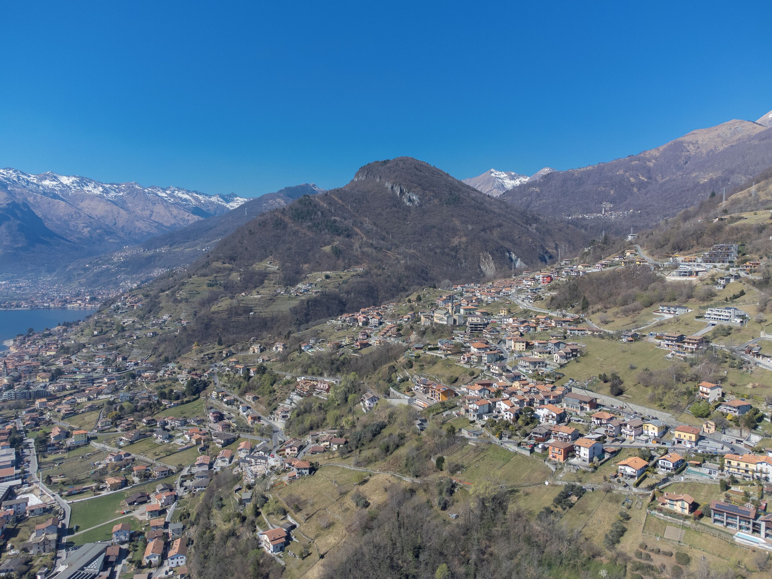 A mountainous town with a mix of residential and commercial buildings, a clear sky, and a lake in the background.