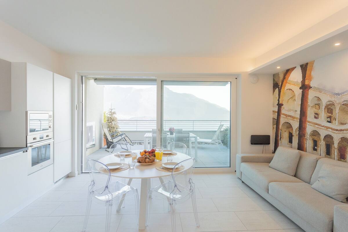 Uma sala de estar moderna com área de jantar, sofá e cozinha com vista para as montanhas.