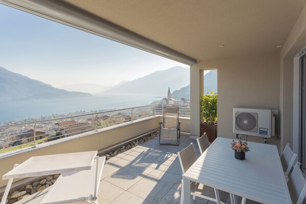 A balcony with a table, chairs, a potted plant, and an air conditioning unit.