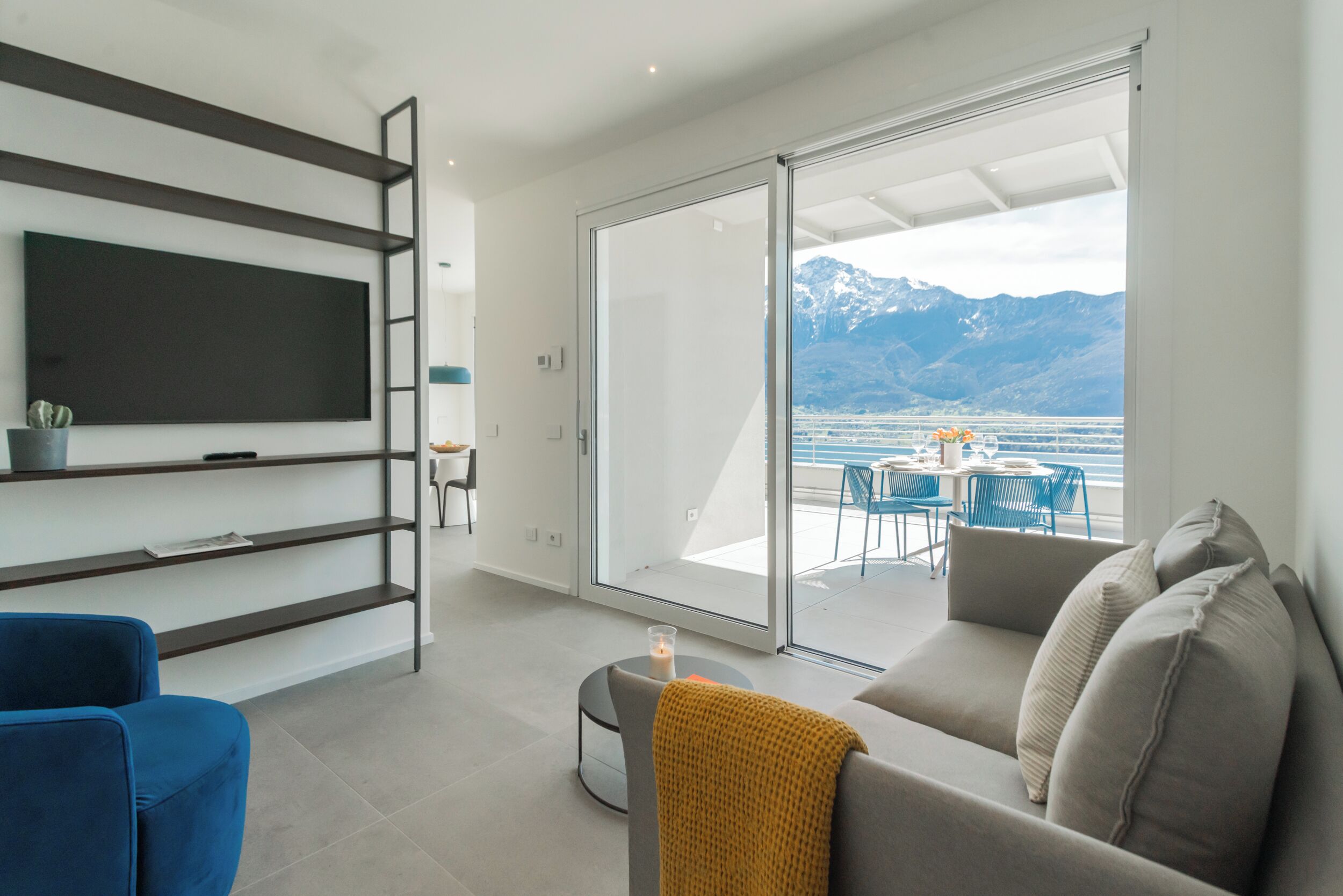 A modern living room with a TV, sofa, and a view of a balcony with a table and chairs.