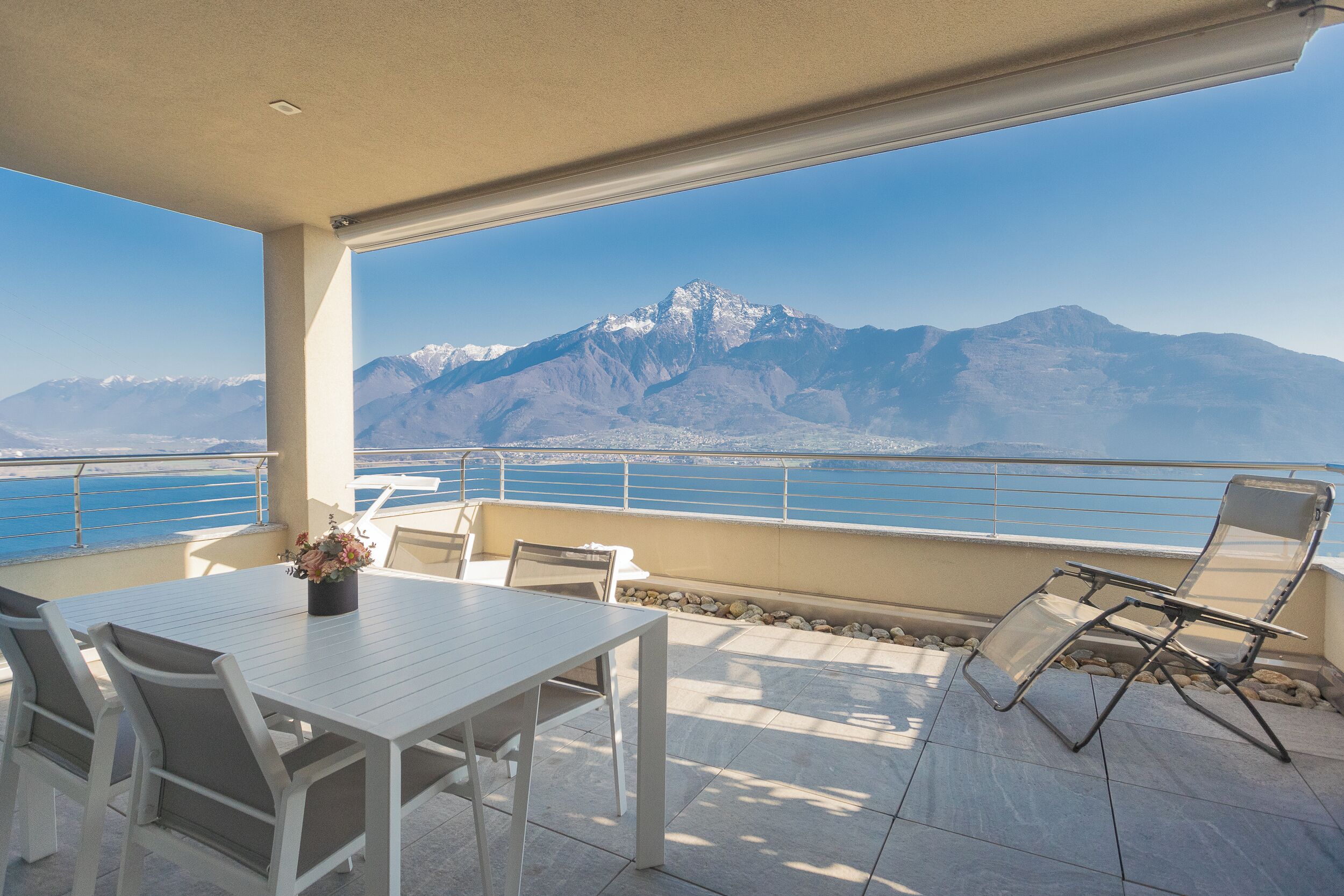 Una terraza con mesa y sillas, vistas a montañas y un cuerpo de agua.