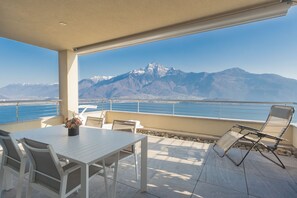 A terrace with a table and chairs, a view of mountains, and a body of water.