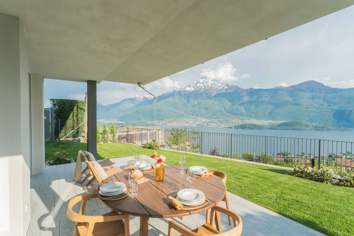 Uma área de refeições com uma mesa posta para quatro, com vista para um lago e montanhas.