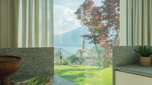 A balcony with a view of a church, a tree with red leaves, and a body of water. - Valarin Luxury Apartments & Wellness by Rent all Como (Vercana)