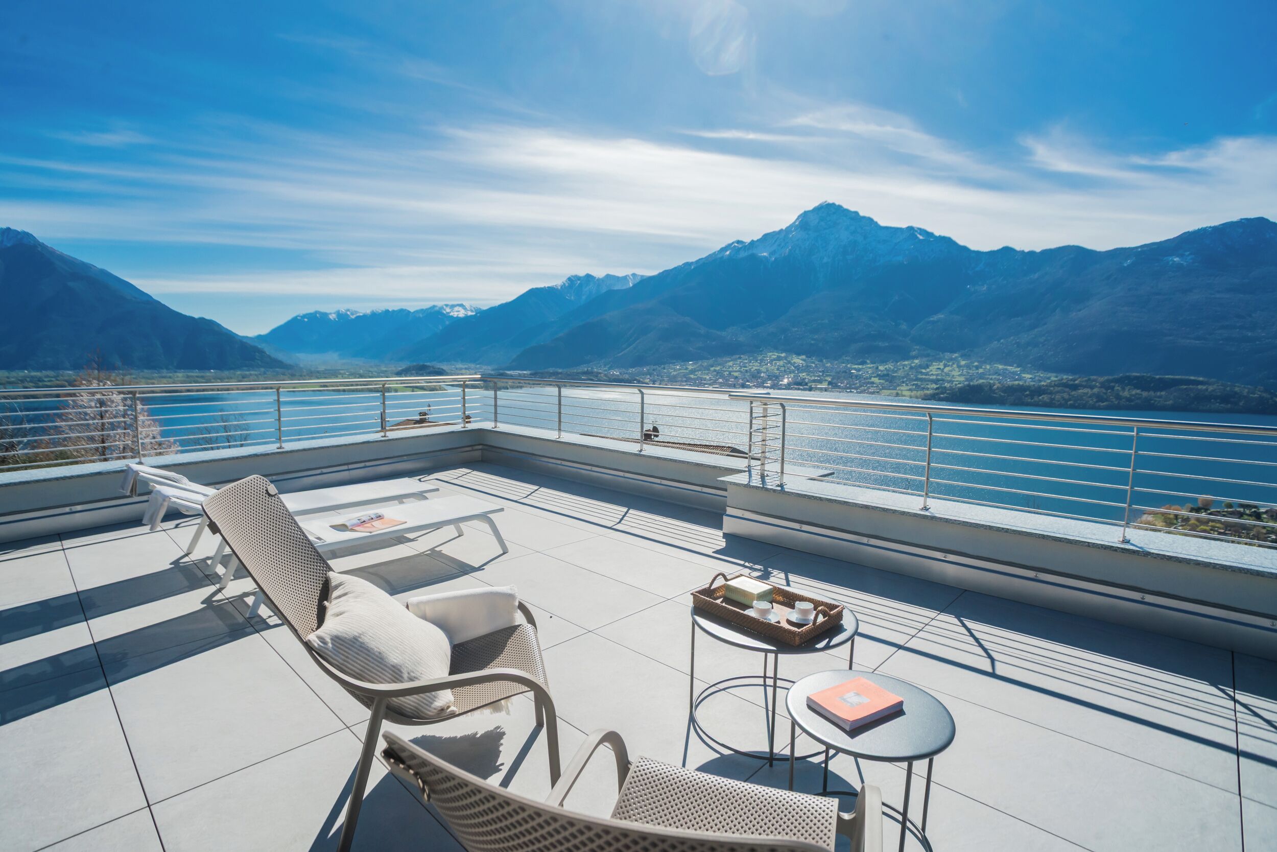 A terrace with chairs and a table, overlooking a lake and mountains.