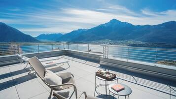 A terrace with chairs and a table, overlooking a lake and mountains.