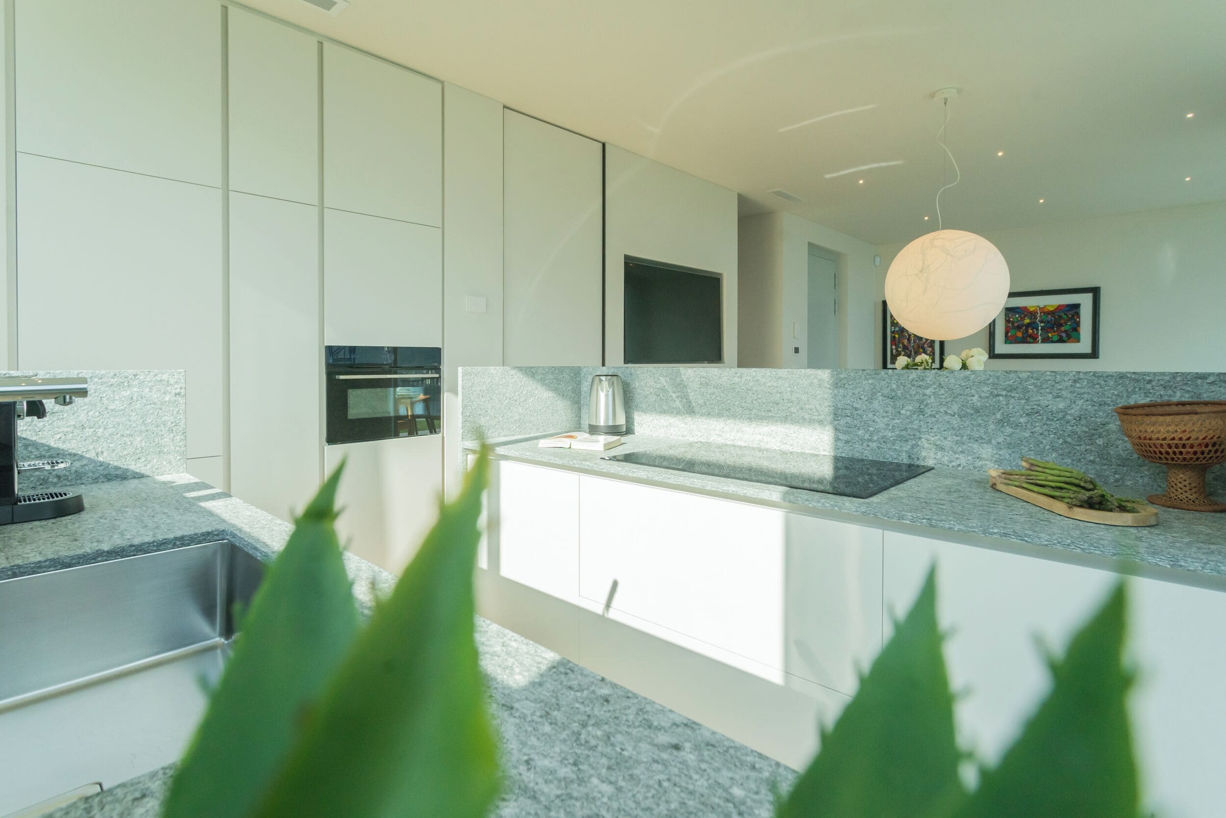 A modern kitchen with white cabinets, a granite countertop, a built-in oven, and a hanging light fixture.