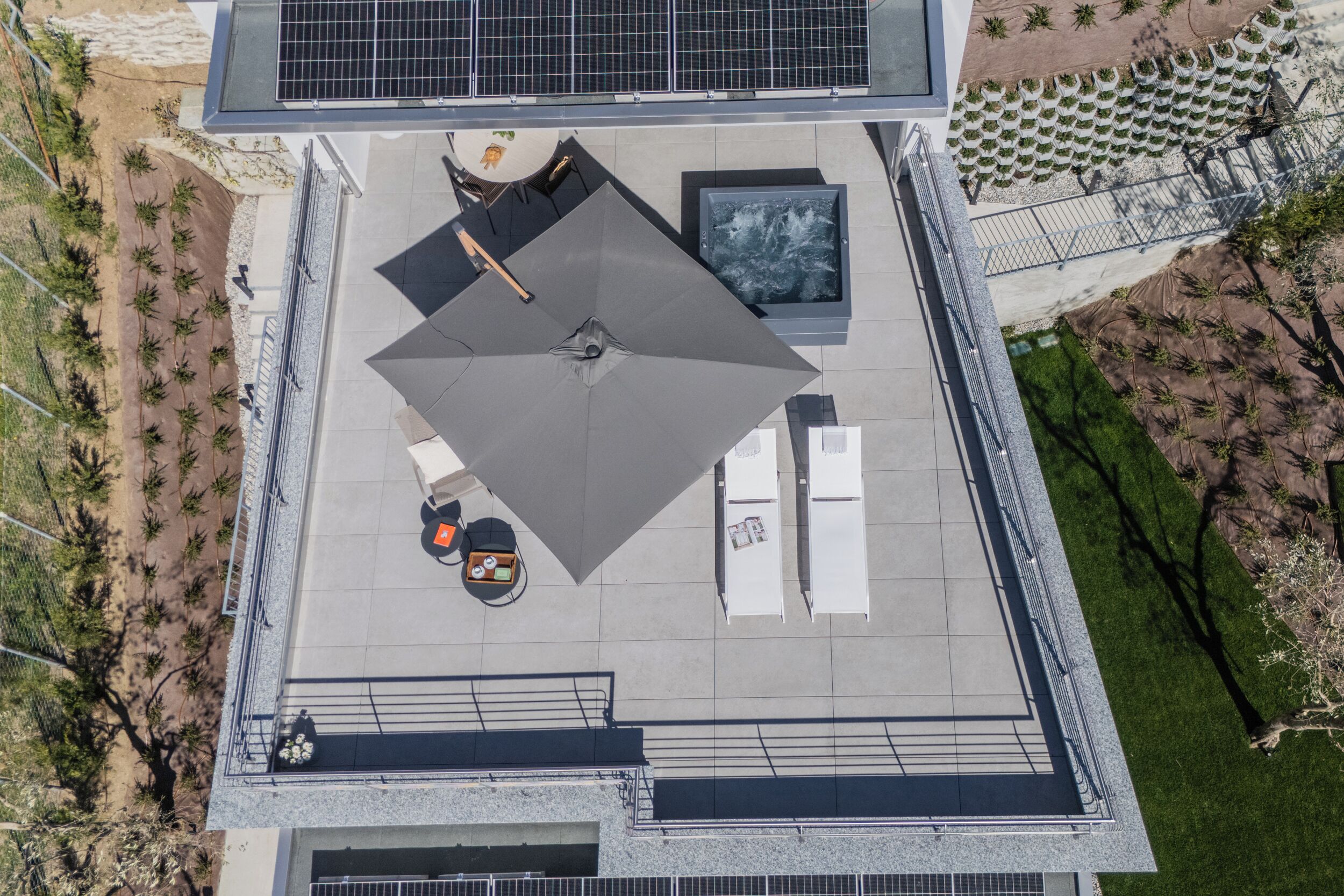 An aerial view of a rooftop terrace with a large umbrella, seating area, and solar panels.
