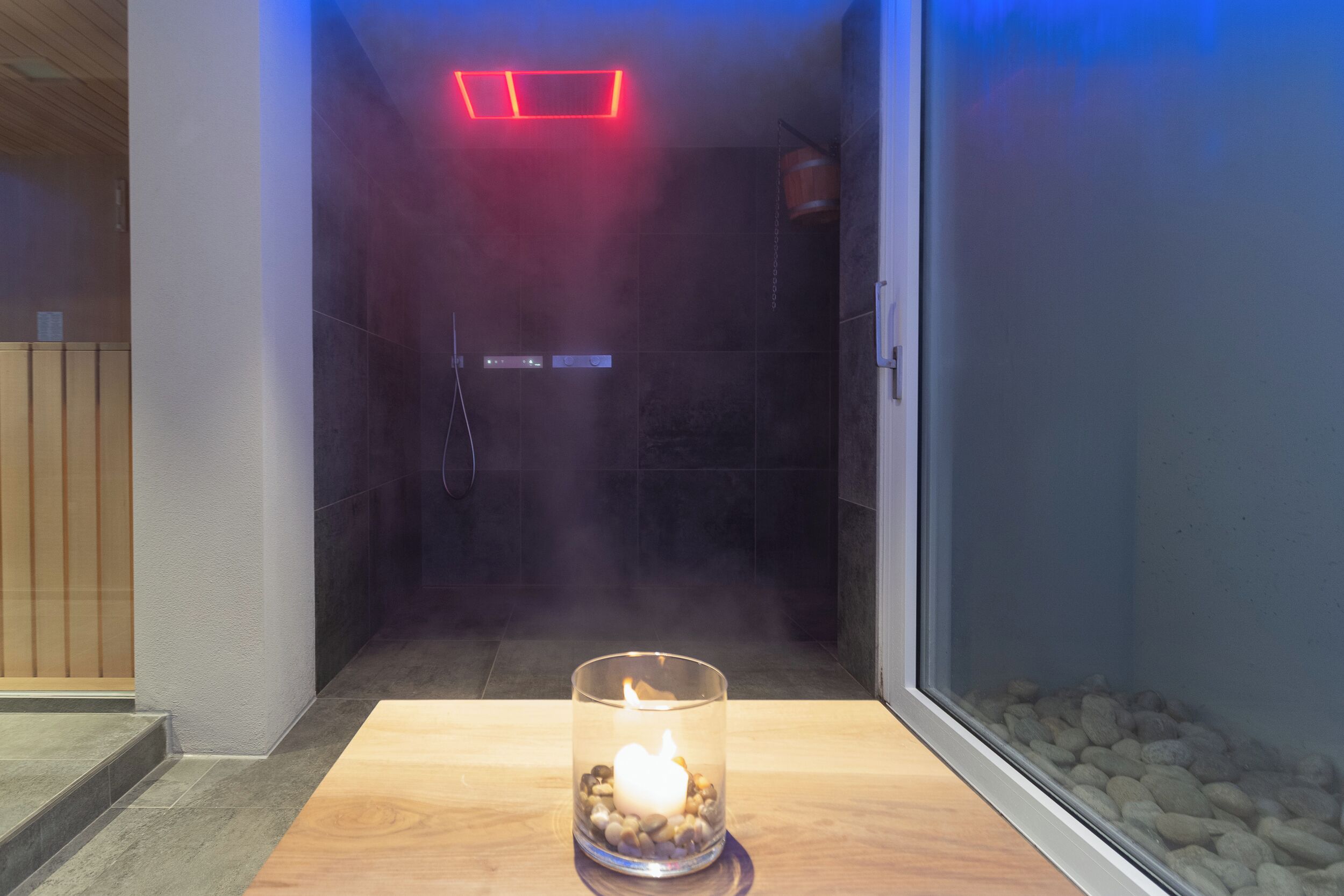 Ein modernes Badezimmer mit Glasabtrennung, einer Kerze und einer roten Leuchte.