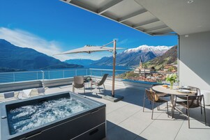 Una terraza en la azotea con hidromasaje, mobiliario exterior y vistas a un lago y montañas.