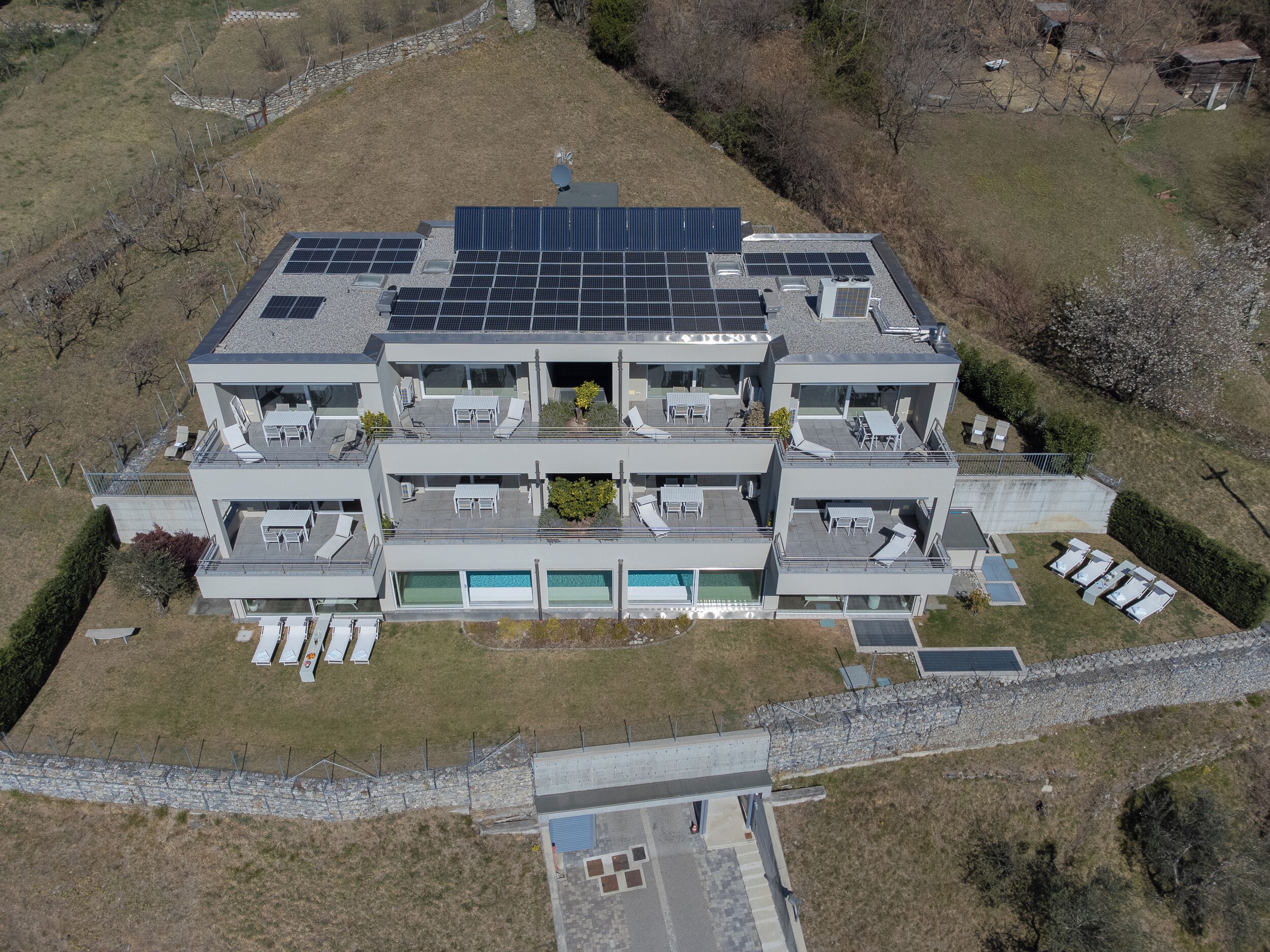 A modern multi-story building with rooftop solar panels, multiple balconies, and a swimming pool.