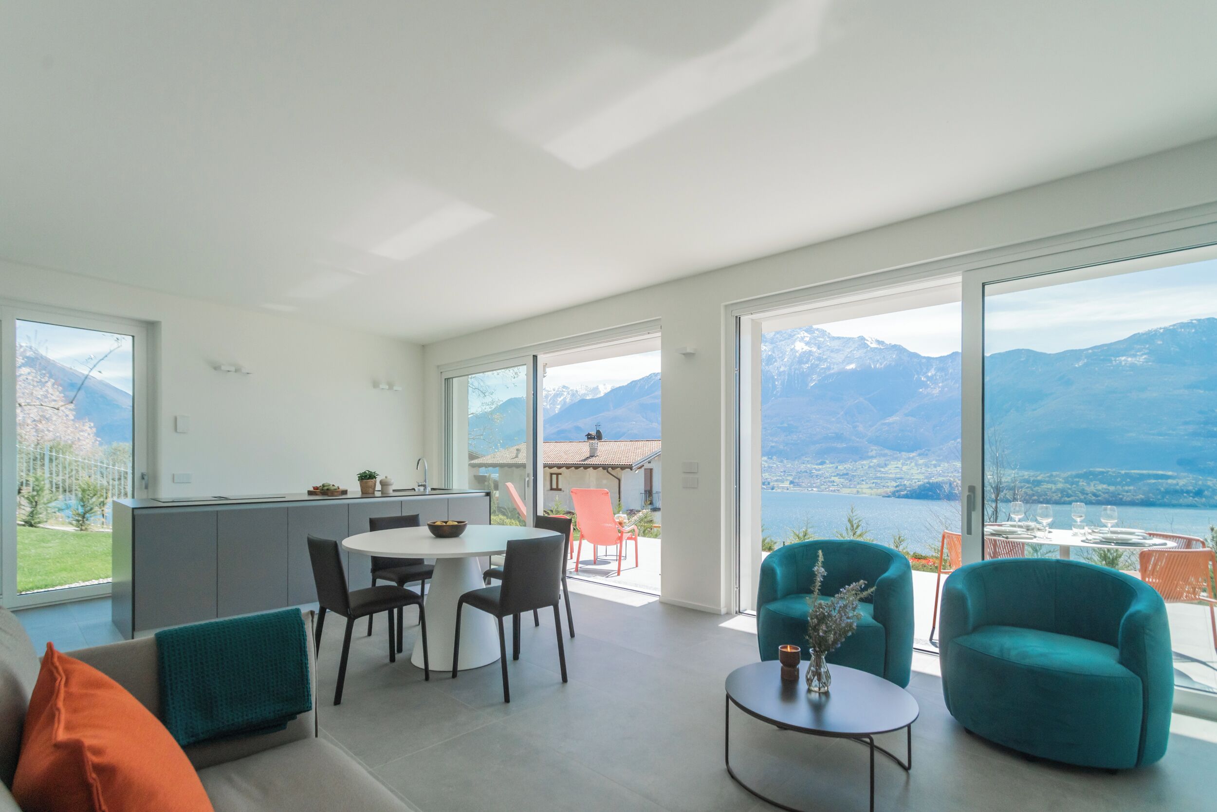 A spacious living area with a kitchen, dining table, and chairs, large windows with a mountain view.
