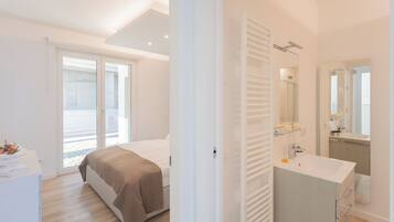 Une chambre à coucher moderne avec un lit, une table de chevet, une grande fenêtre et une salle de bain équipée d’un lavabo et d’un miroir.