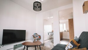 En moderne stue med et fladskærms-tv, en sofa, et sofabord og et spiseområde i baggrunden.
