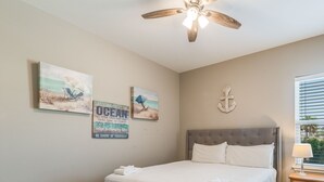 A bedroom with a bed, a ceiling fan, artwork on the wall, and a window with blinds.