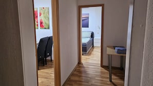 Un couloir étroit, doté d’un plancher en bois, mène à une chambre à coucher qui contient un lit et une table de chevet.