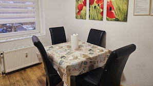Un coin repas avec une table dressée pour quatre personnes, un radiateur en dessous et une fenêtre avec des stores.