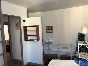 Un bany amb un lavabo blanc, un mirall, una barra de tovalloles i una estant amb una làmpada.