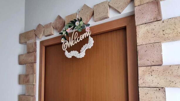 Een houten deur met een 'Welcome'-bord erboven, omringd door een bakstenen muur.
