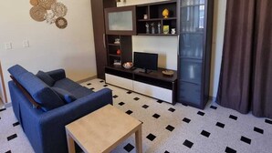 Een woonkamer met een blauwe bank, een klein houten tafeltje en een tv-meubel met planken.