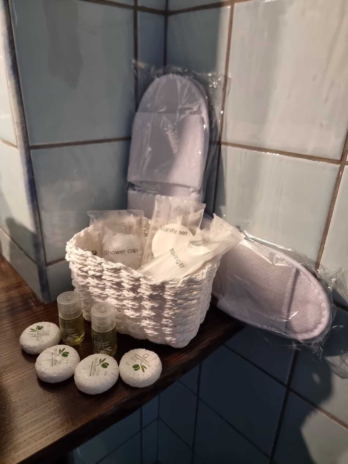 Ein Badezimmerbereich mit Duschhaube, einem weißen gewebten Korb mit Pflegeprodukten und drei runden Flaschen auf einem Holzboden.
