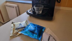 Een koffieapparaat op een keukentafel met twee zakjes koffie en een glas.
